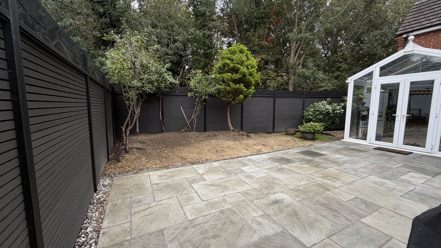 Black garden fencing and a paved patio beside a conservatory, completed by Inova Garden
